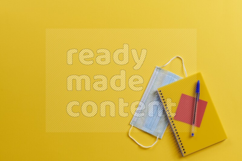 A yellow notebook with different school supplies on yellow background