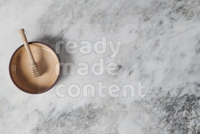 Beige pottery oven plate with wooden honey dipper in it on grey marble background