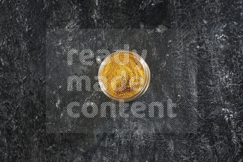 وعاء زجاجي ممتلئ ببودرة الكركم على خلفية سوداء