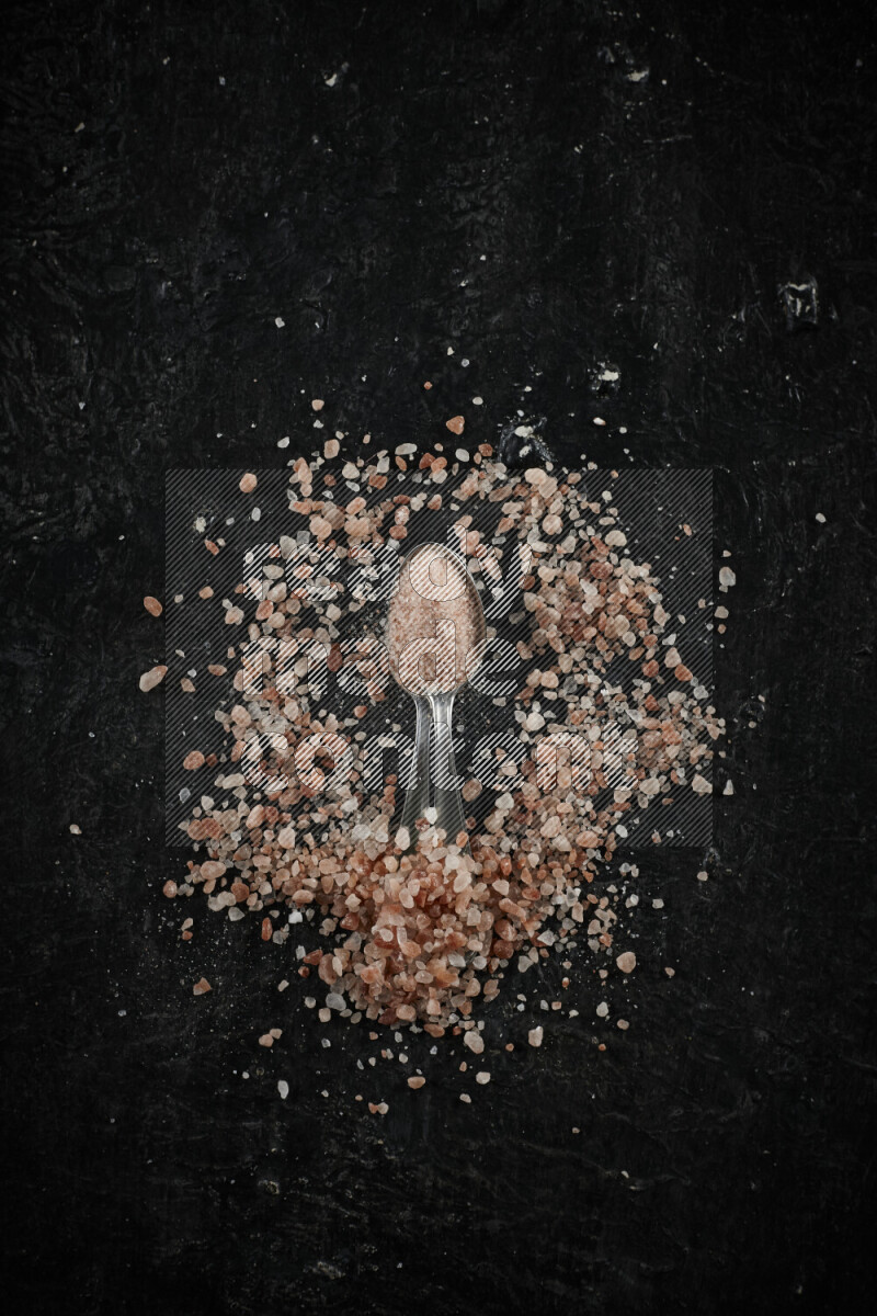 2 metal spoons filled with pink himalayan salt on black background