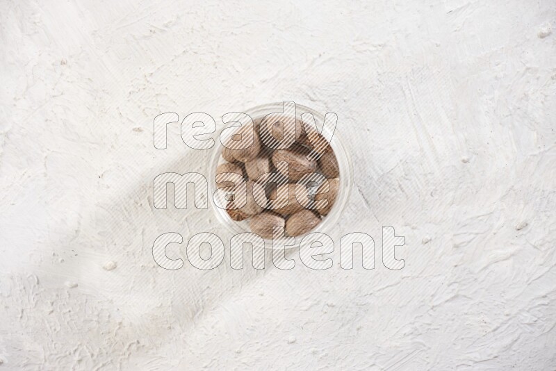 A glass jar full of whole nutmeg seeds on a white flooring