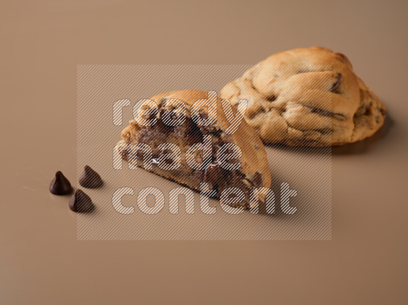 a chocolate chip cookie with another one cut in half on a brown background