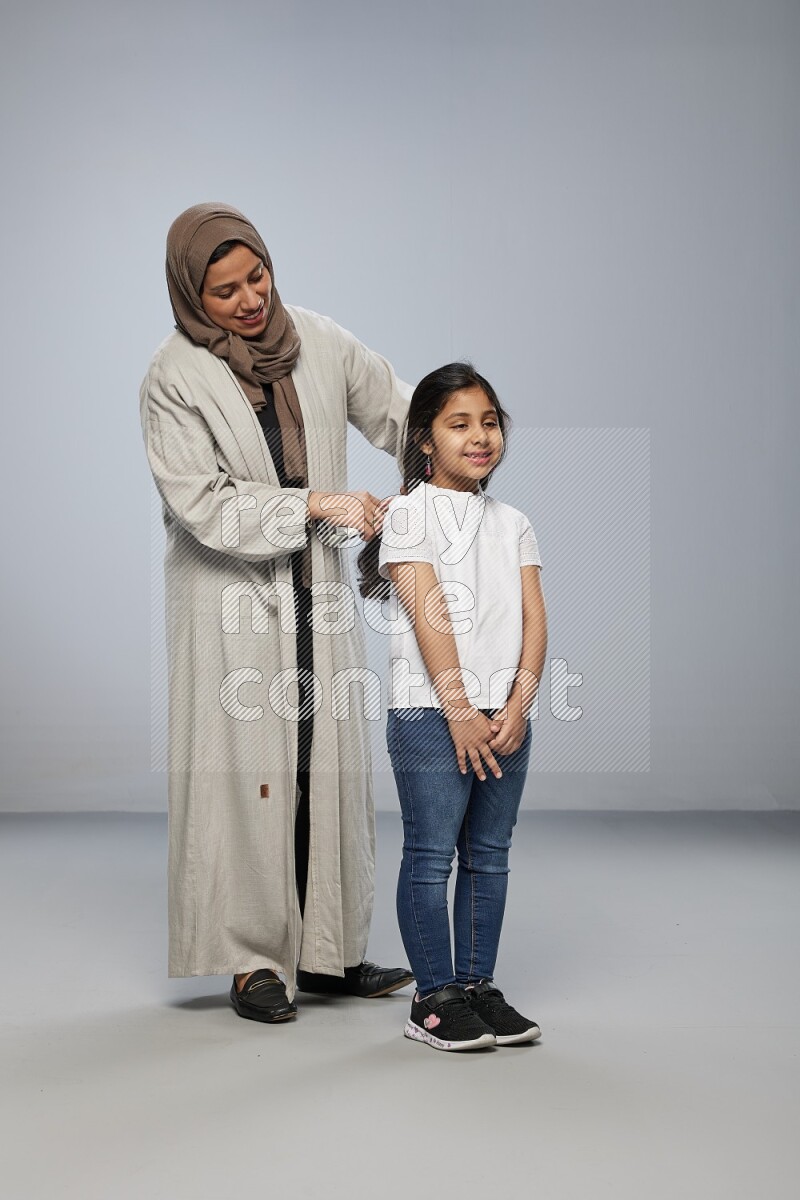 Mom standing styling hair for her daughter on gray background