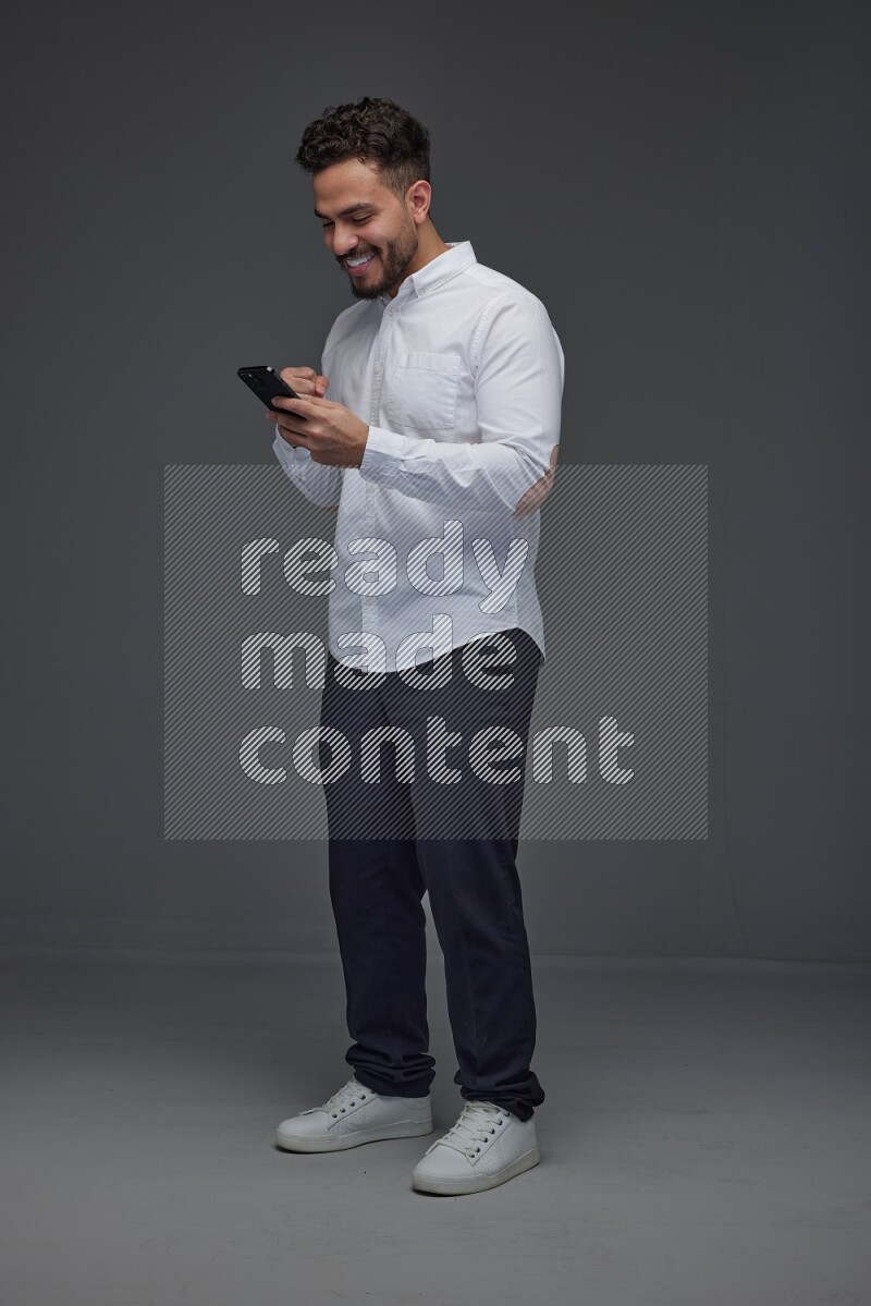A man wearing smart casual standing and using his phone eye level on a gray background