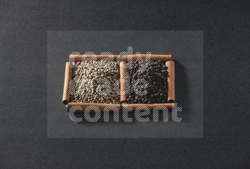 مربعان من أعواد القرفة ممتلئان بحبوب الفلفل الأبيض وحبوب الفلفل الأسود علي خلفية سوداء