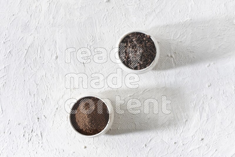 2 Beige ceramic bowls, one full of cloves and the other full of powder on textured white flooring