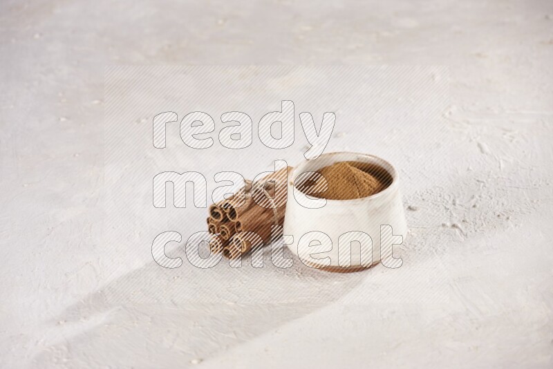 Cinnamon sticks stacked and bounded beside a beige bowl full of cinnamon powder on white background
