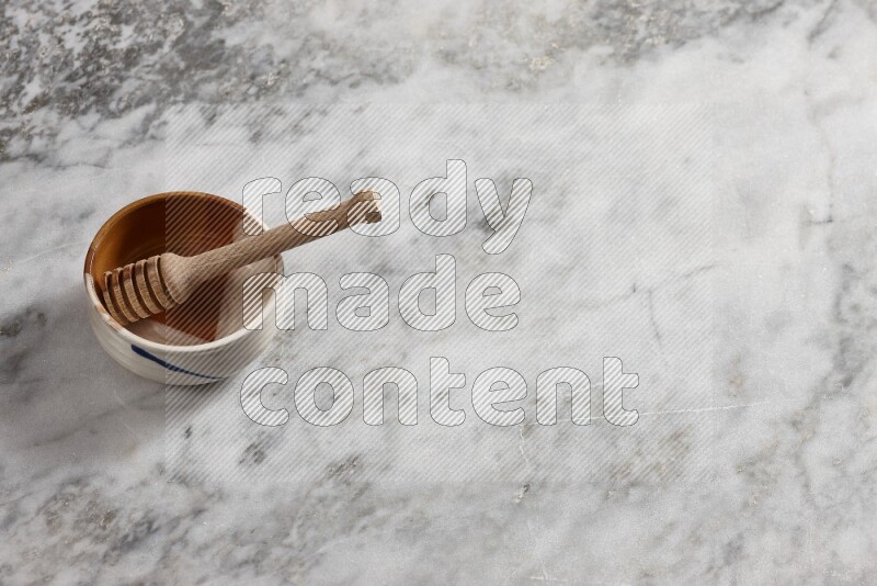 Multicolored pottery bowl with wooden honey dipper in it on grey marble background
