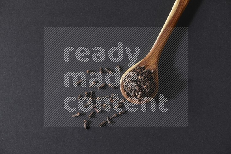 A wooden ladle full of whole cloves on a black flooring