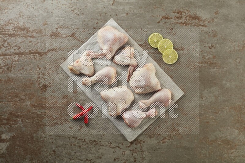 Mixed fresh chicken pieces on a parchment paper direct on a textured rustic background