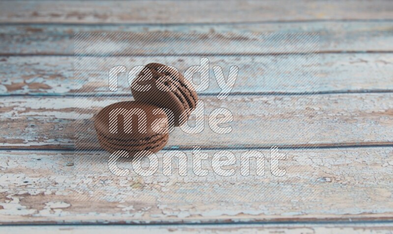 45º Shot of two Brown Dark Chocolate macarons on light blue wooden background