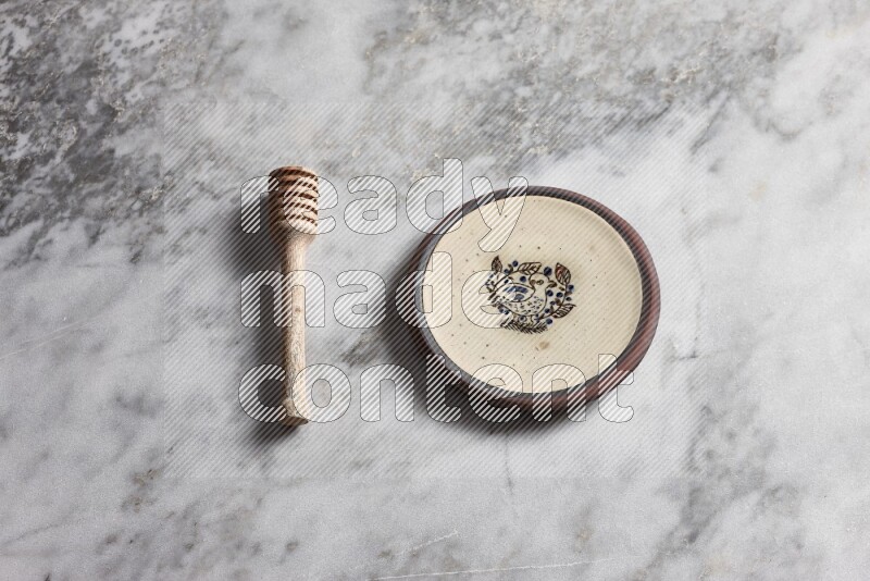 Decorative pottery plate with wooden honey dipper on the side on grey marble background