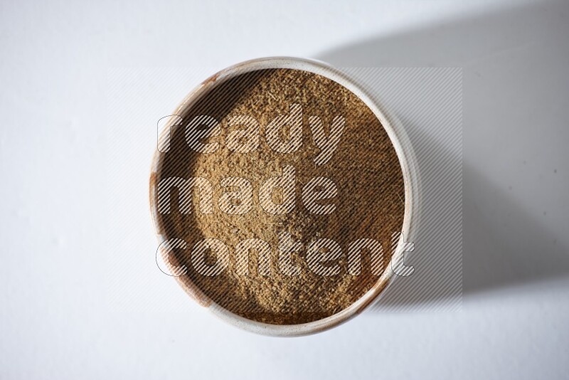 وعاء بيج ممتلئ ببودرة الكمون على خلفية بيضاء