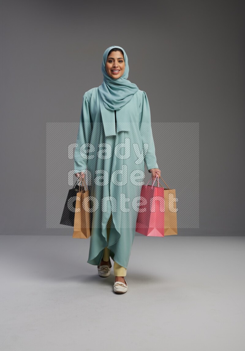 Saudi Woman wearing Abaya standing holding shopping bag on Gray background