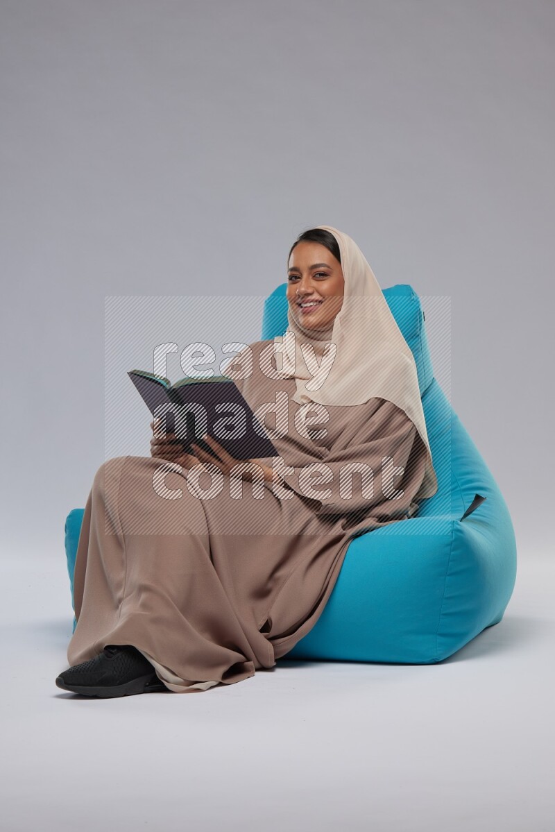 A woman sitting on a blue beanbag and reading a book