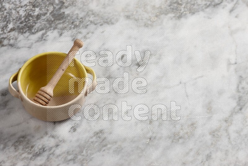 Multicolored pottery bowl with wooden honey dipper in it on grey marble background