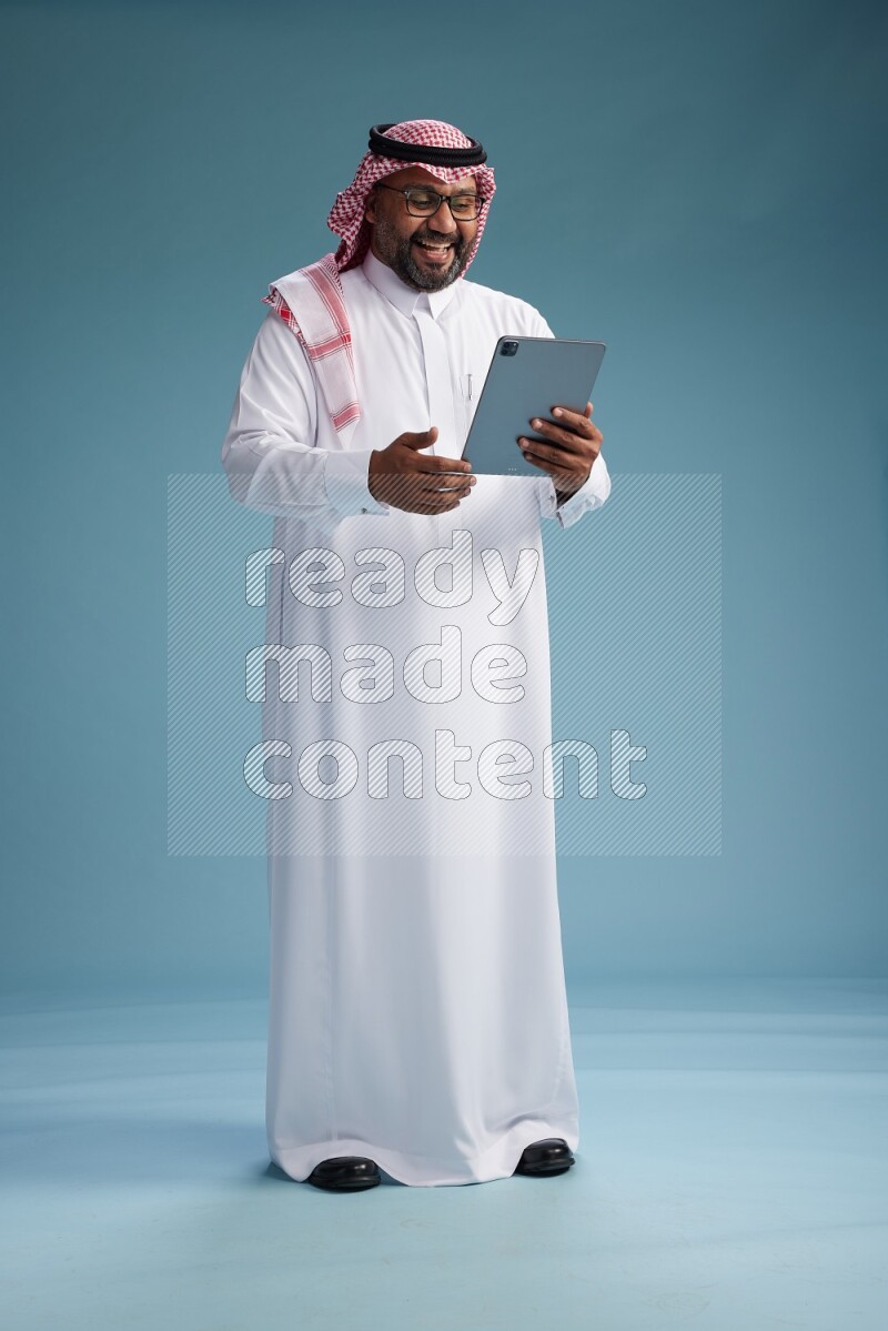 Saudi Man with shimag Standing holding a tablet on blue background