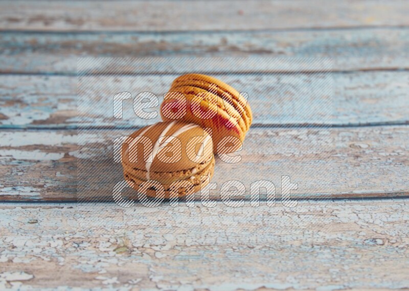 45º Shot of of two assorted Brown Irish Cream, and Orange Exotic macarons on light blue background