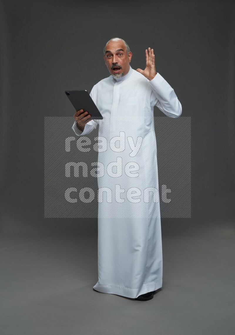 Saudi man without shomag Standing working on tablet on gray background