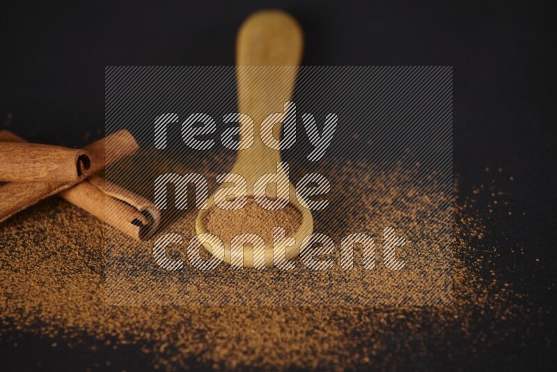 Cinnamon powder in a wooden spoon and cinnamon sticks beside it on black background