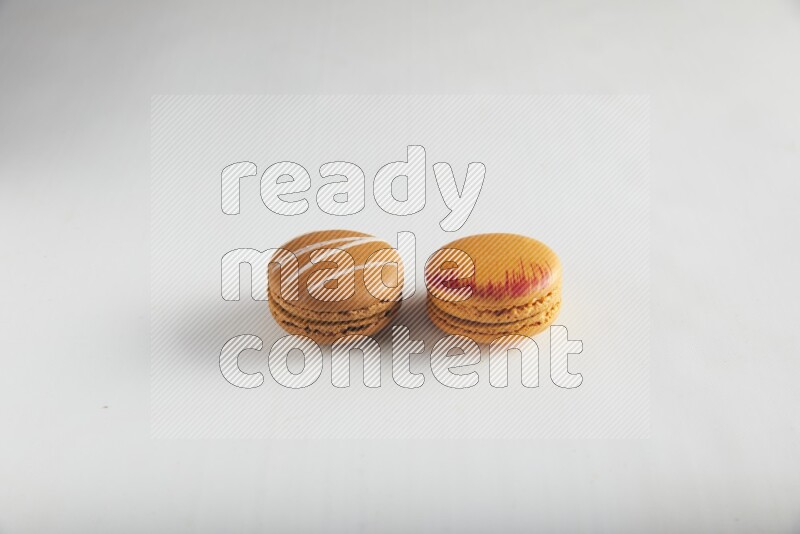 45º Shot of of two assorted Brown Irish Cream, and Orange Exotic macarons on white background