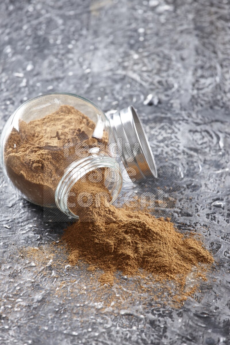 Flipped herbal glass jar full of cinnamon powder on textured black background