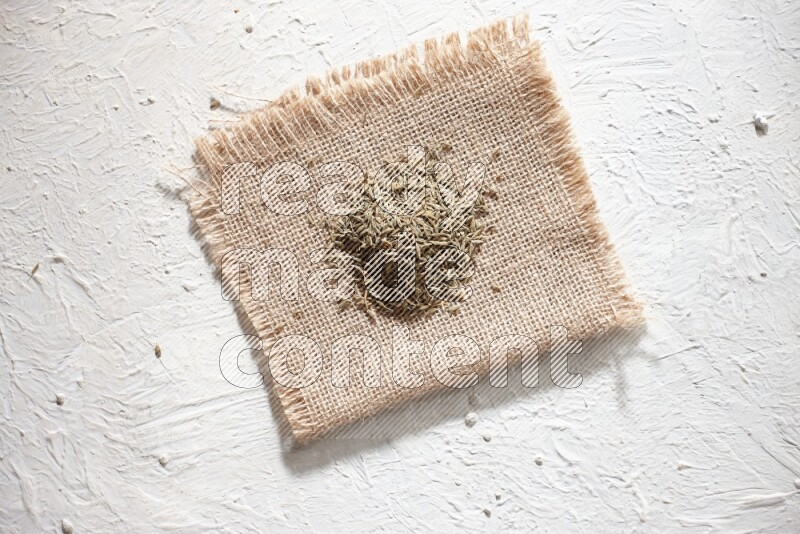 Cumin seeds on a burlap piece on a textured white flooring