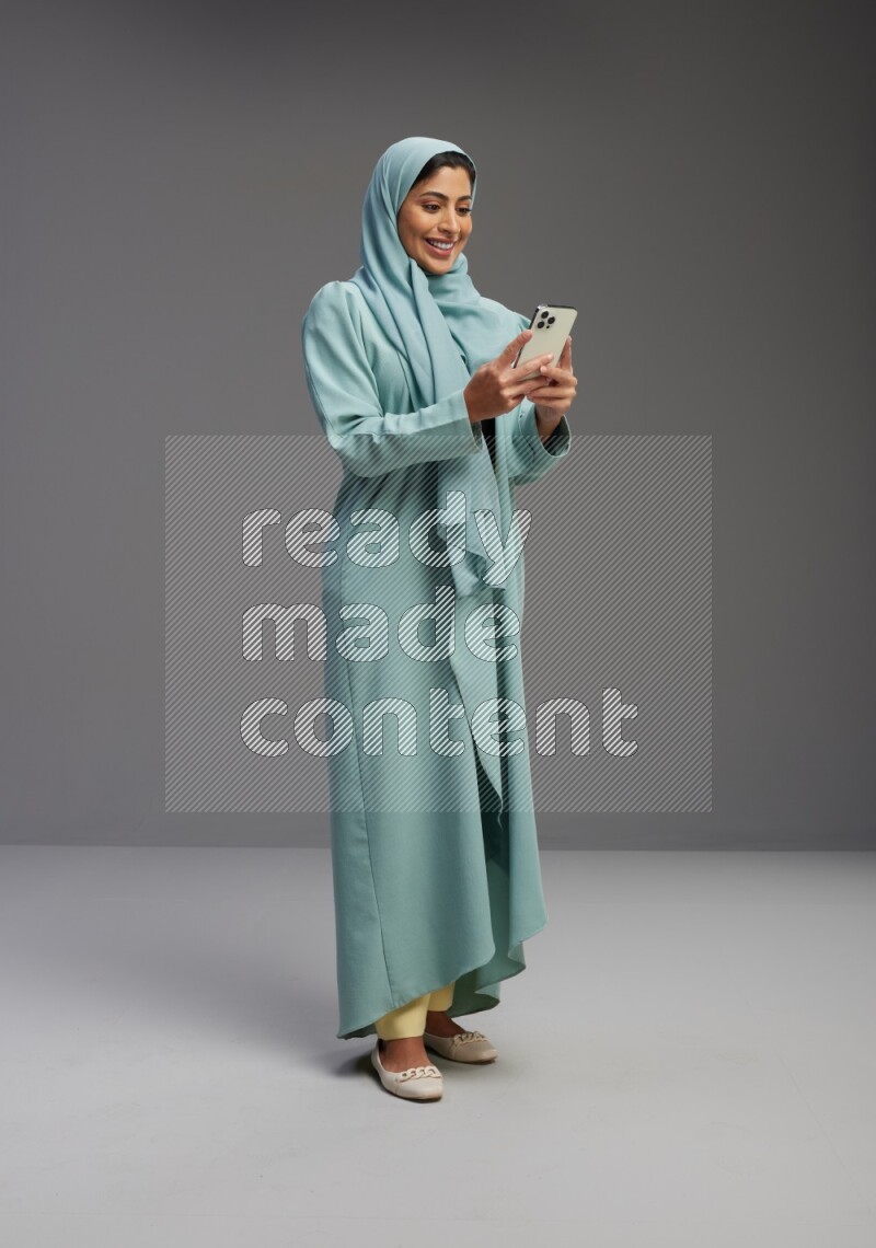 Saudi Woman wearing Abaya standing texting on phone on Gray background