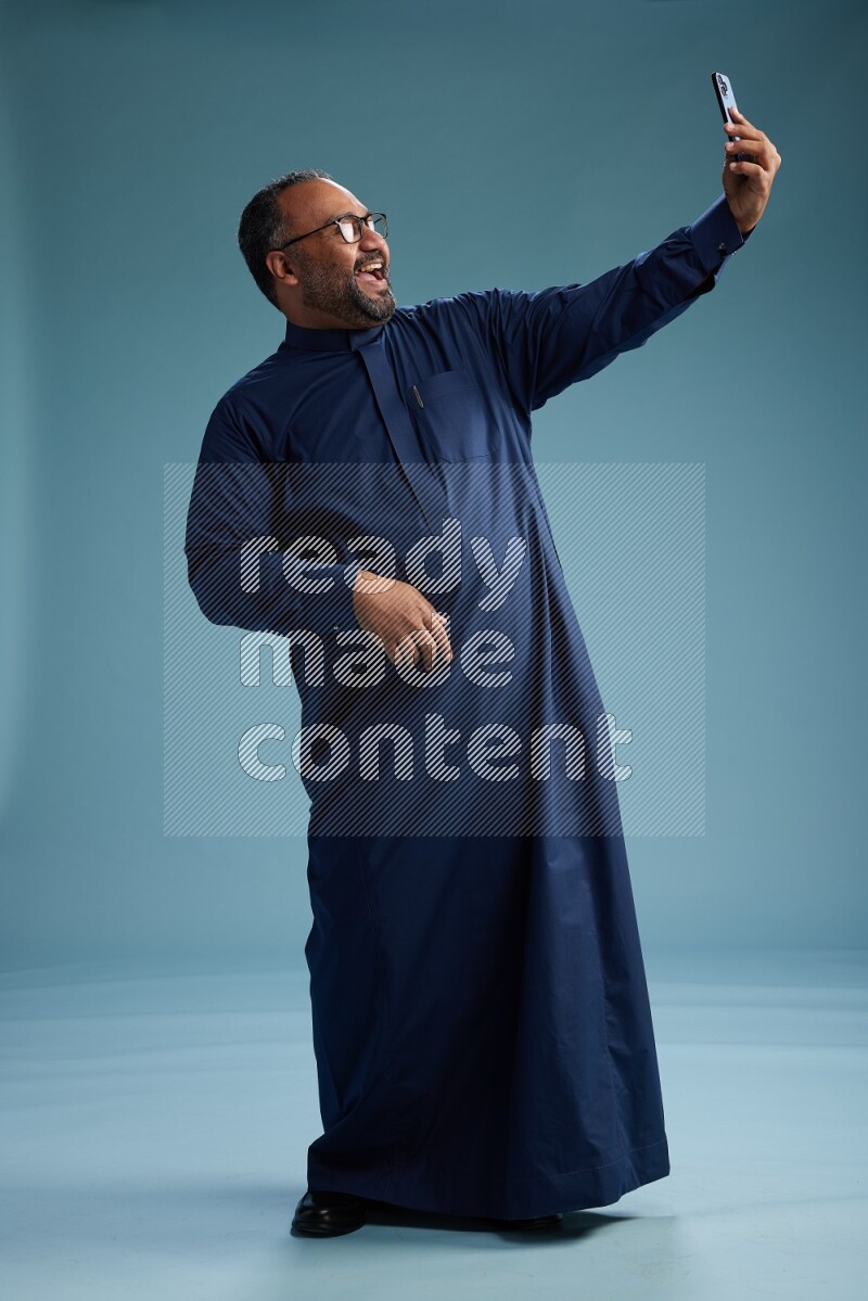 Saudi Man without shimag Standing taking selfie on blue background