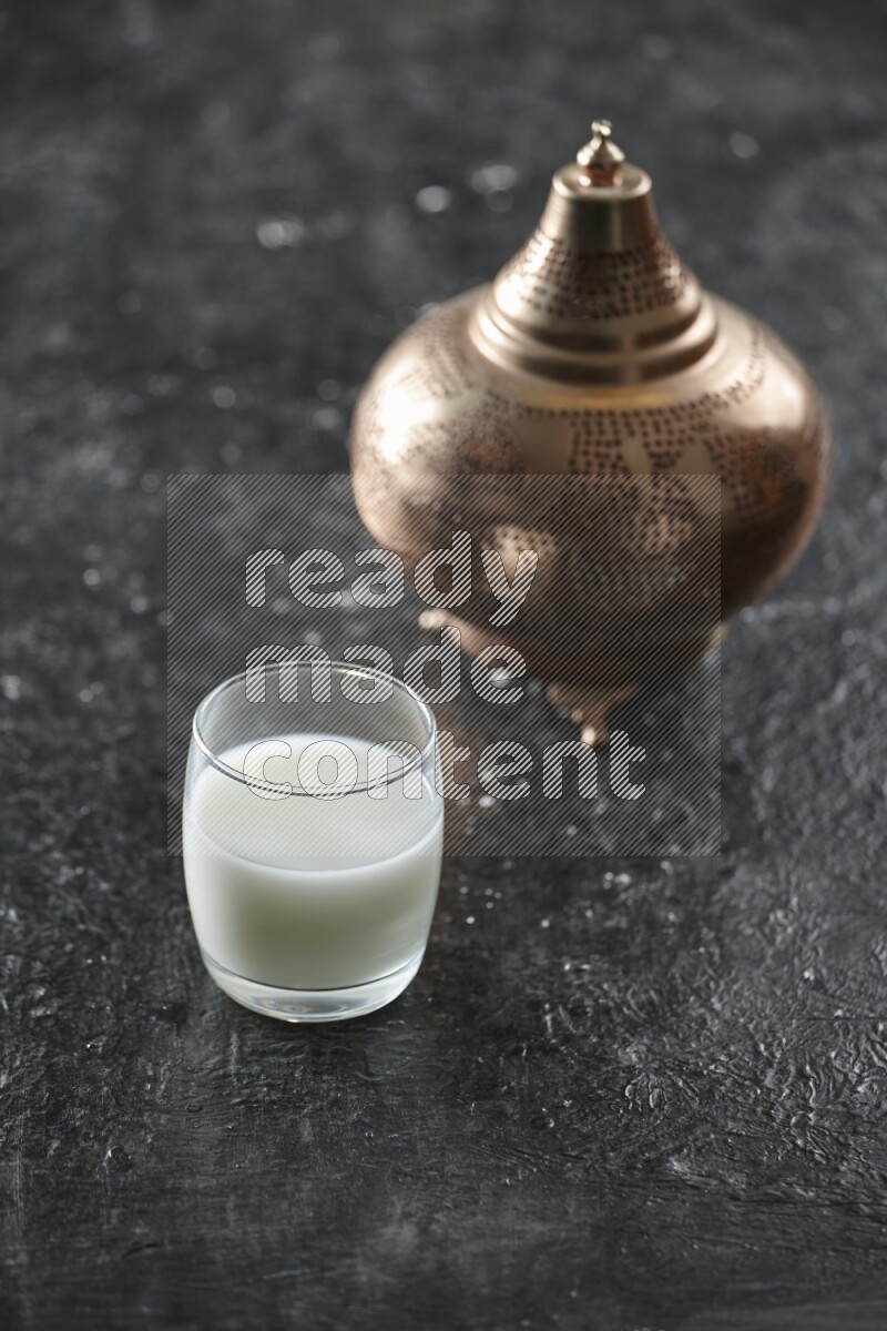 A golden lantern with different drinks, dates, nuts, prayer beads and quran on textured black background