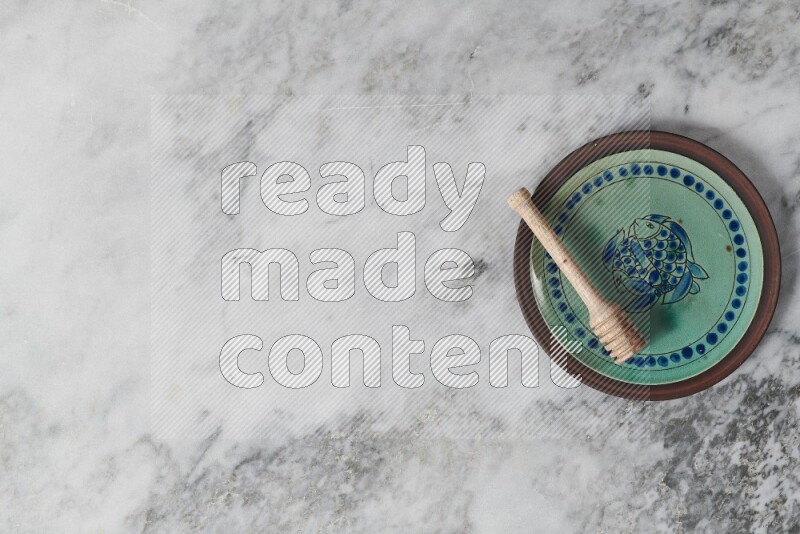 Decorative pottery plate with wooden honey dipper in it on grey marble background