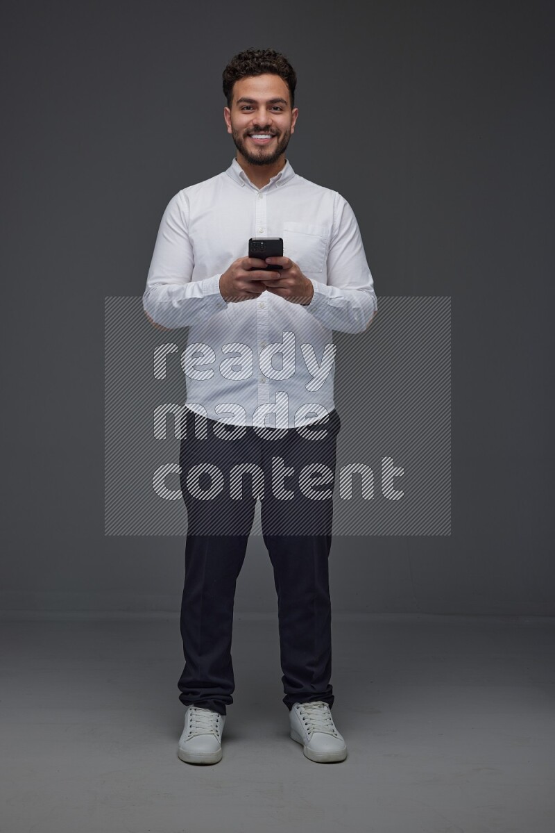 A man wearing smart casual standing and using his phone eye level on a gray background