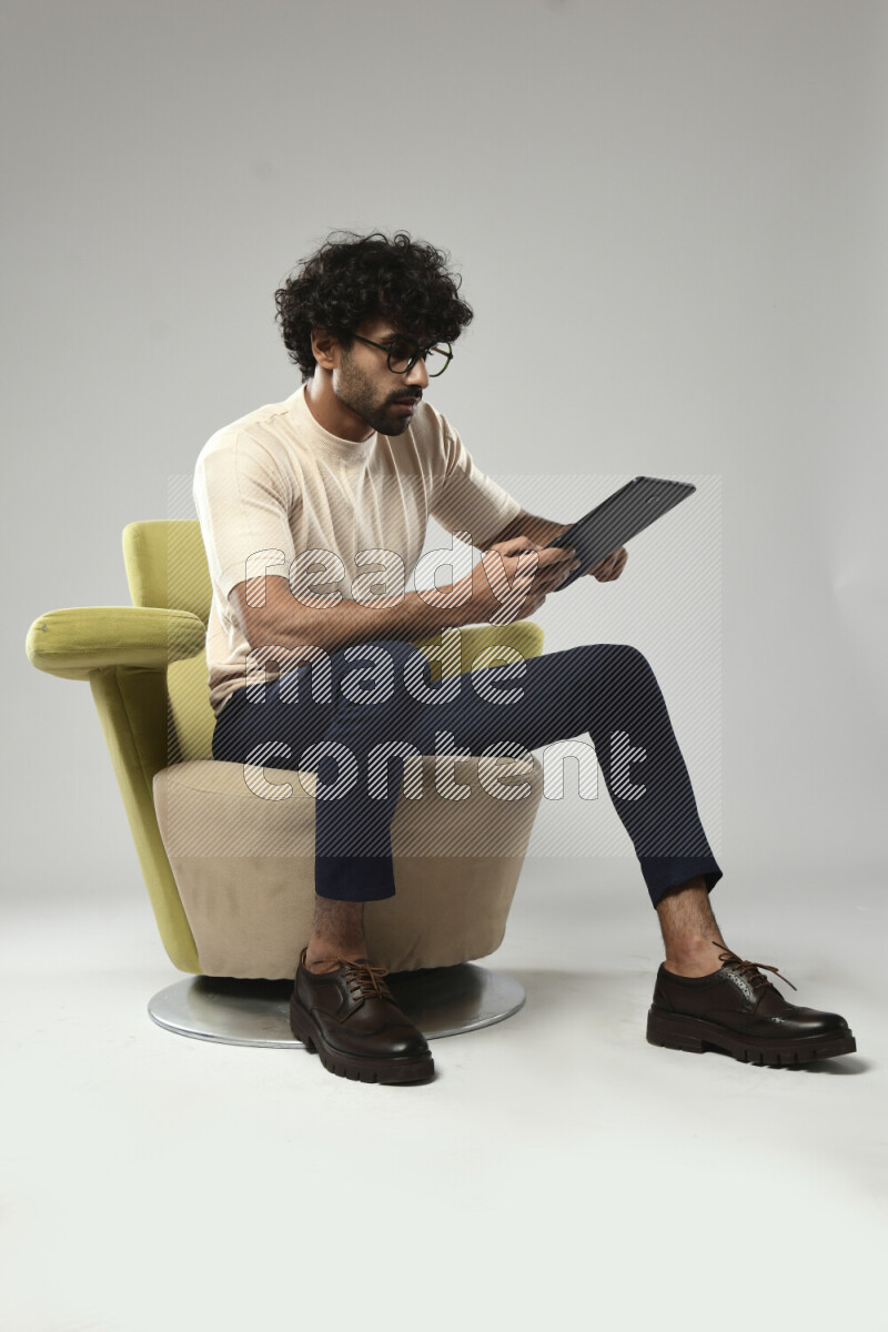 A man wearing casual sitting on a chair browsing on a tablet on white background