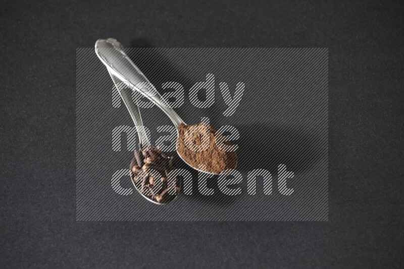 ملعقتان معدنيتان، إحداهما ممتلئة بحبوب القرنفل والأخرى ببودرة القرنفل، على خلفية سوداء