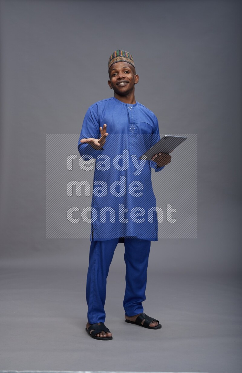 Man wearing Nigerian outfit standing working on tablet on gray background