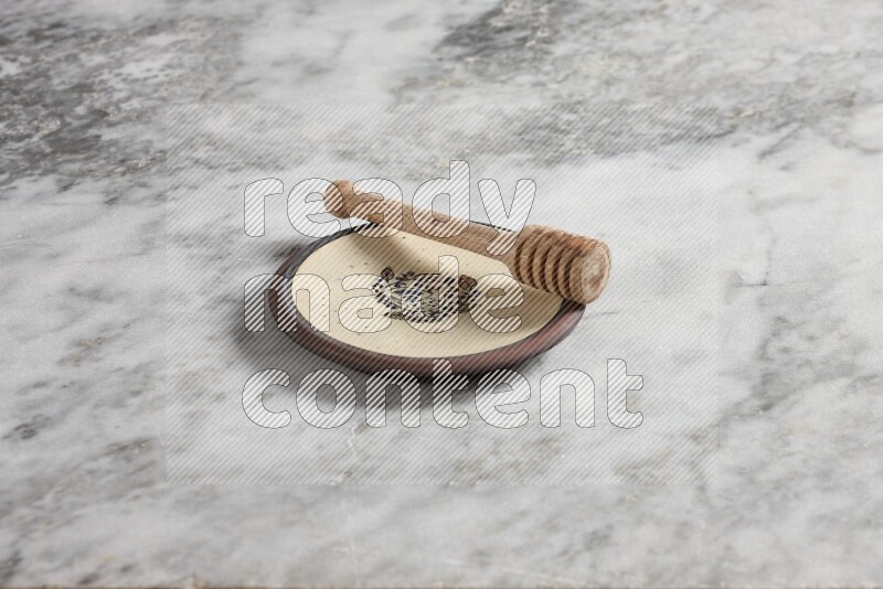 Decorative pottery plate with wooden honey dipper in it on grey marble background