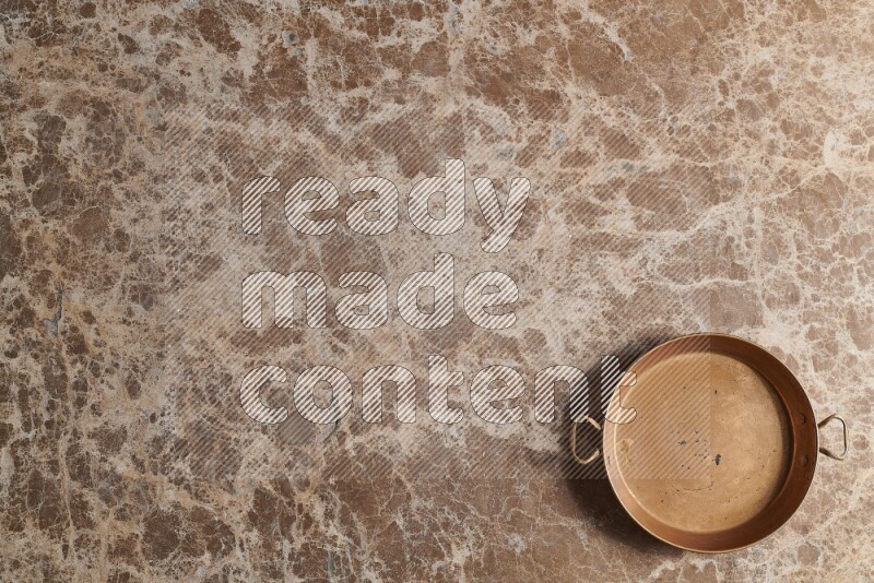 A small copper pan on beige marble background