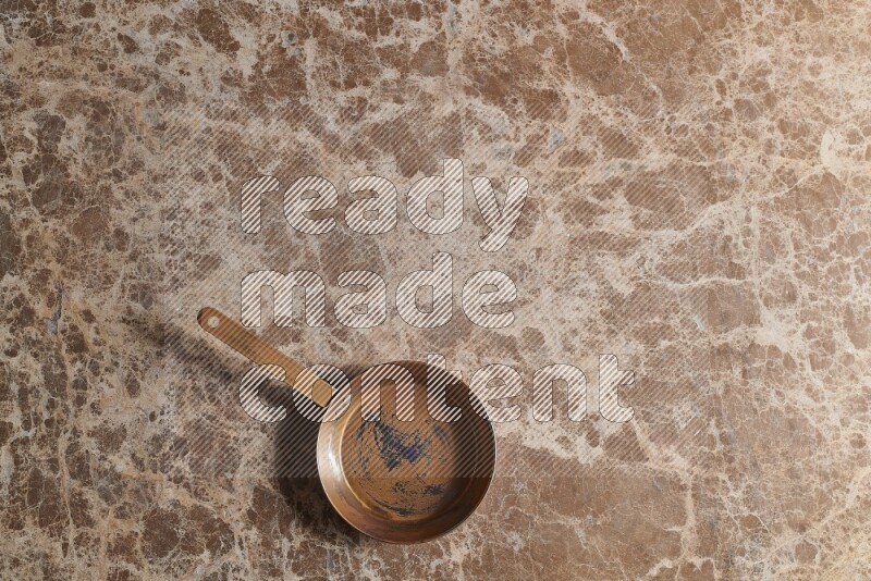 A small copper pan on beige marble background