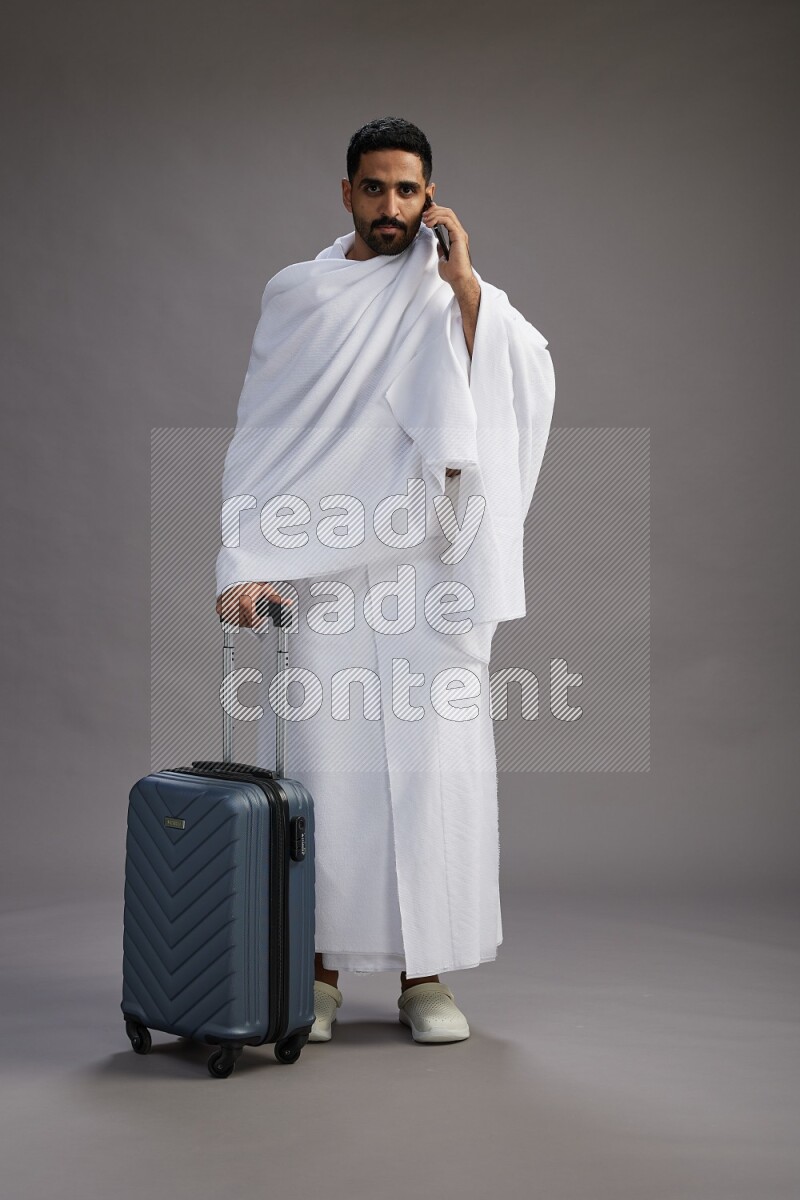 A man wearing Ehram Standing holding traveling bag on gray background