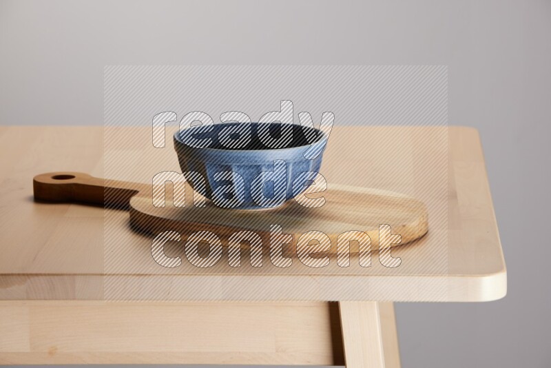 blue bowl placed on a  wooden oval cutting board on the edge of wooden table