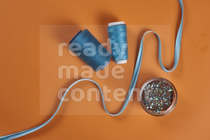A blue collection of sewing and tailoring tools arranged on a orange background