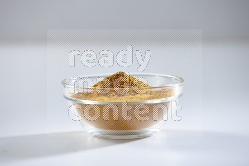 A glass bowl full of turmeric powder on white flooring