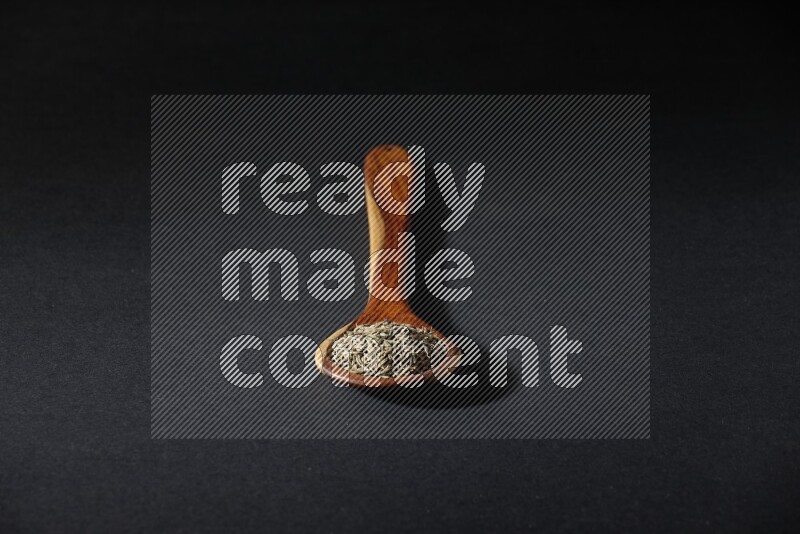 A wooden ladle full of cumin seeds on black flooring