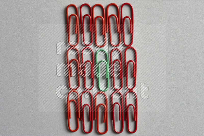 A bunch of red paper clips with a different colored paper clip in the center on grey background