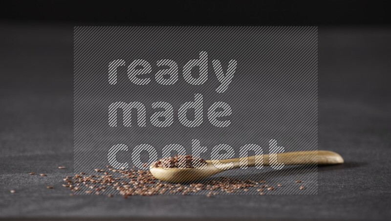 ملعقة خشبية ممتلئة بحبوب بذر الكتان وبعض البذور متناثرة علي خلفية سوداء