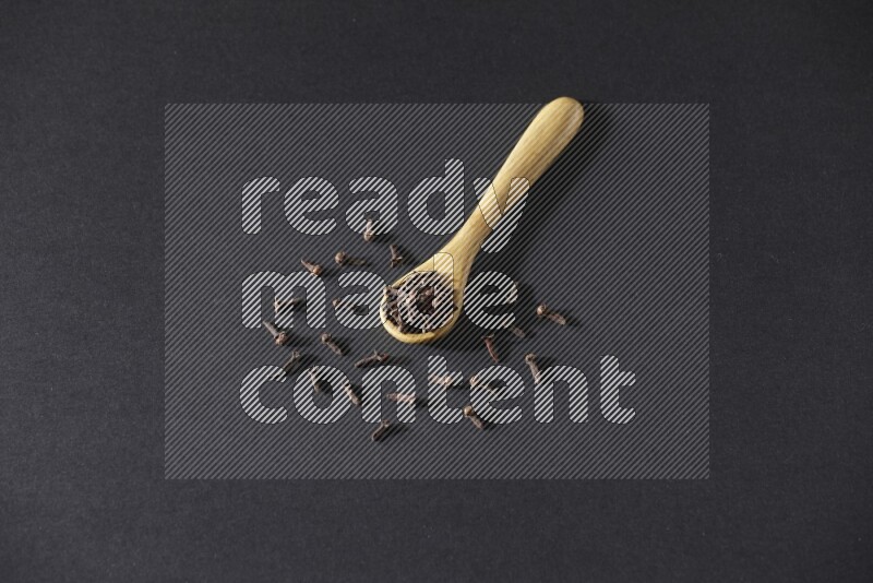 حبوب القرنفل في ملعقة خشبية وبعض من الحبوب تناثرت بخارجها علي خلفية سوداء