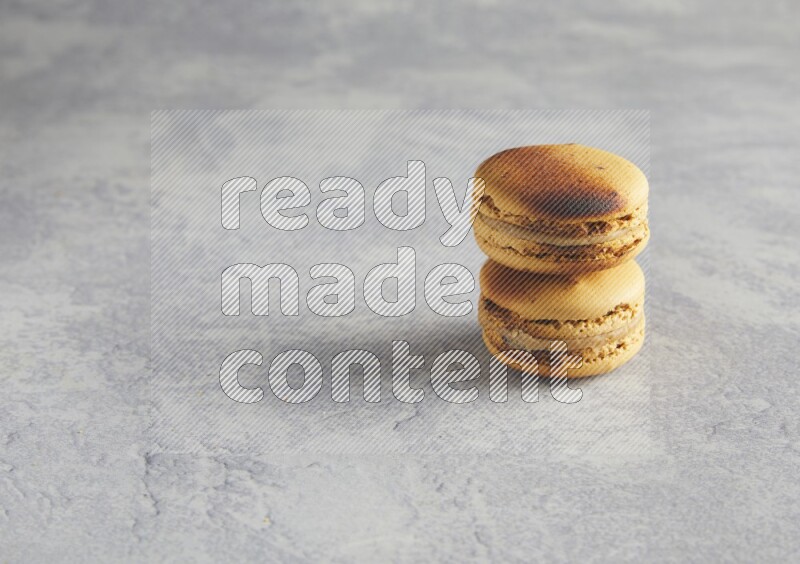 45º Shot of two Yellow Crème Brulée macarons on white  marble background