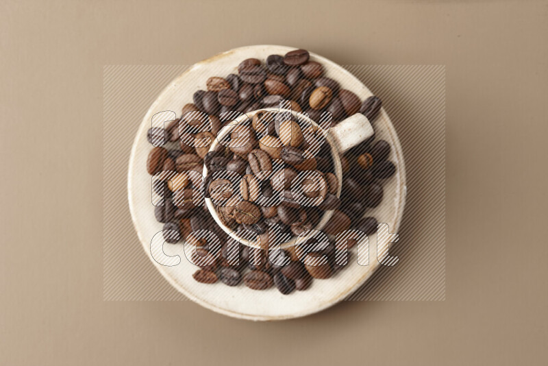 A beige pottery cup full of roasted coffee beans on beige background