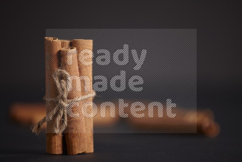 4 Cinnamon sticks stacked and bounded with more sticks in the background on black flooring