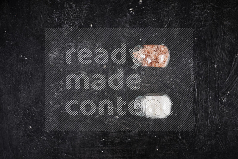 2 glass jars one is filled with coarse himalayan salt and the other with coarse sea salt on black background